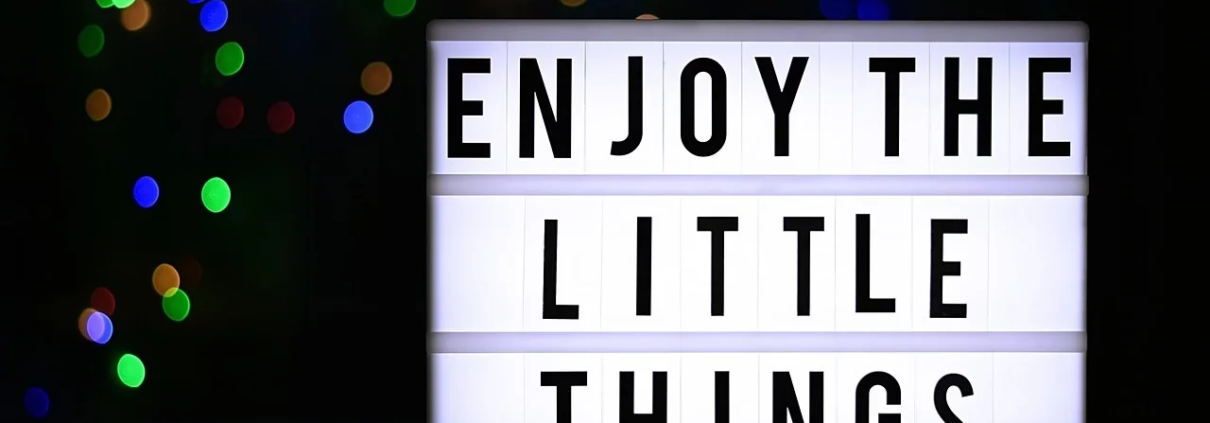Zeigt eine Leuchttafel auf der steht "Enjoy the little things"