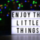 Zeigt eine Leuchttafel auf der steht "Enjoy the little things"