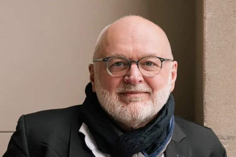 Joseph Pelrine - ein älterer Mann mit Brille und weißem Kurzhaar-Bart. Er trägt zudem einen Schal.