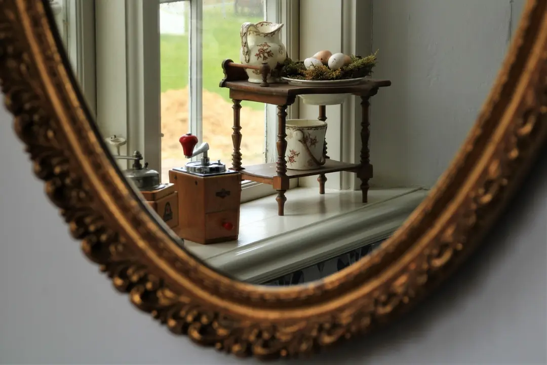 Ein dekorativer Spiegelrahmen spiegelt ein Fenster mit einer Holzablage, auf der eine Kaffeemühle, Geschirr und Eier stehen.
