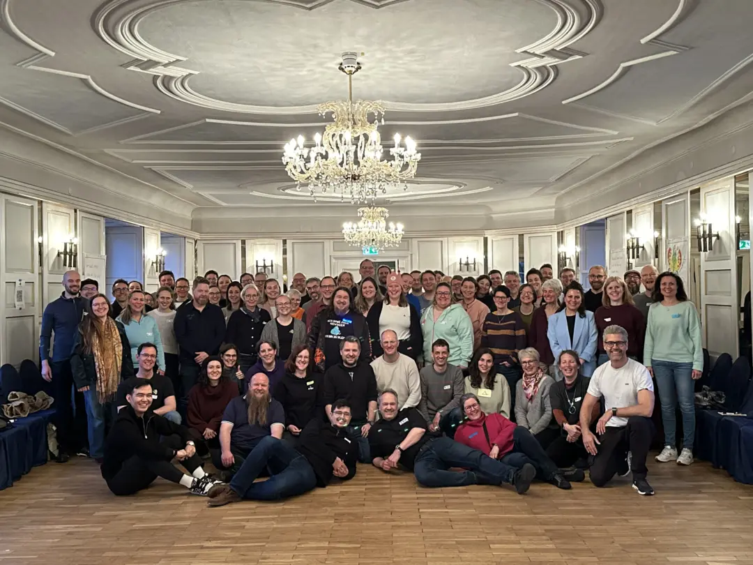 ca. 87 Menschen auf einem Gruppenfoto in einem Saal mit Kronleuchtern