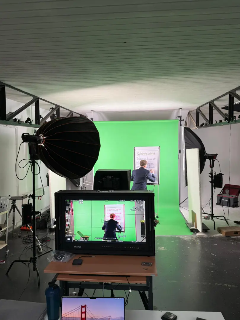 Ralph schreibt am Flipchart vor einem Greenscreen. Im Vordergrund ein Monitor.