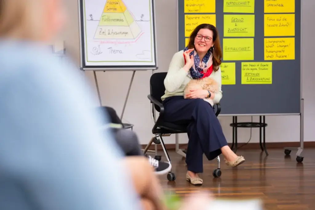 Veronika sitzt vor einer Pinnwand, auf der sind die Haltungen & Prinzipien vom Lösungsfokus